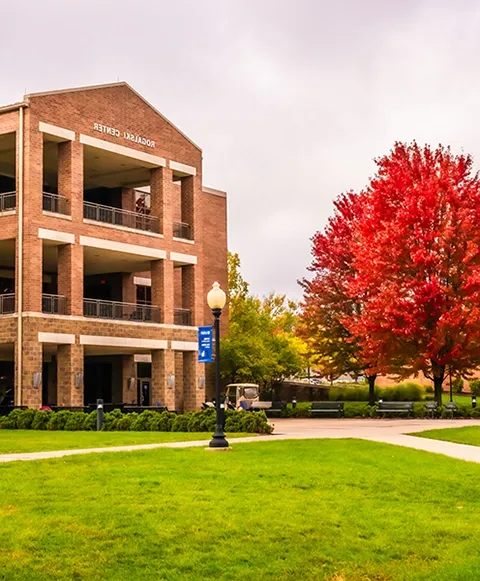 A red tree nexxt to a brick building that says 